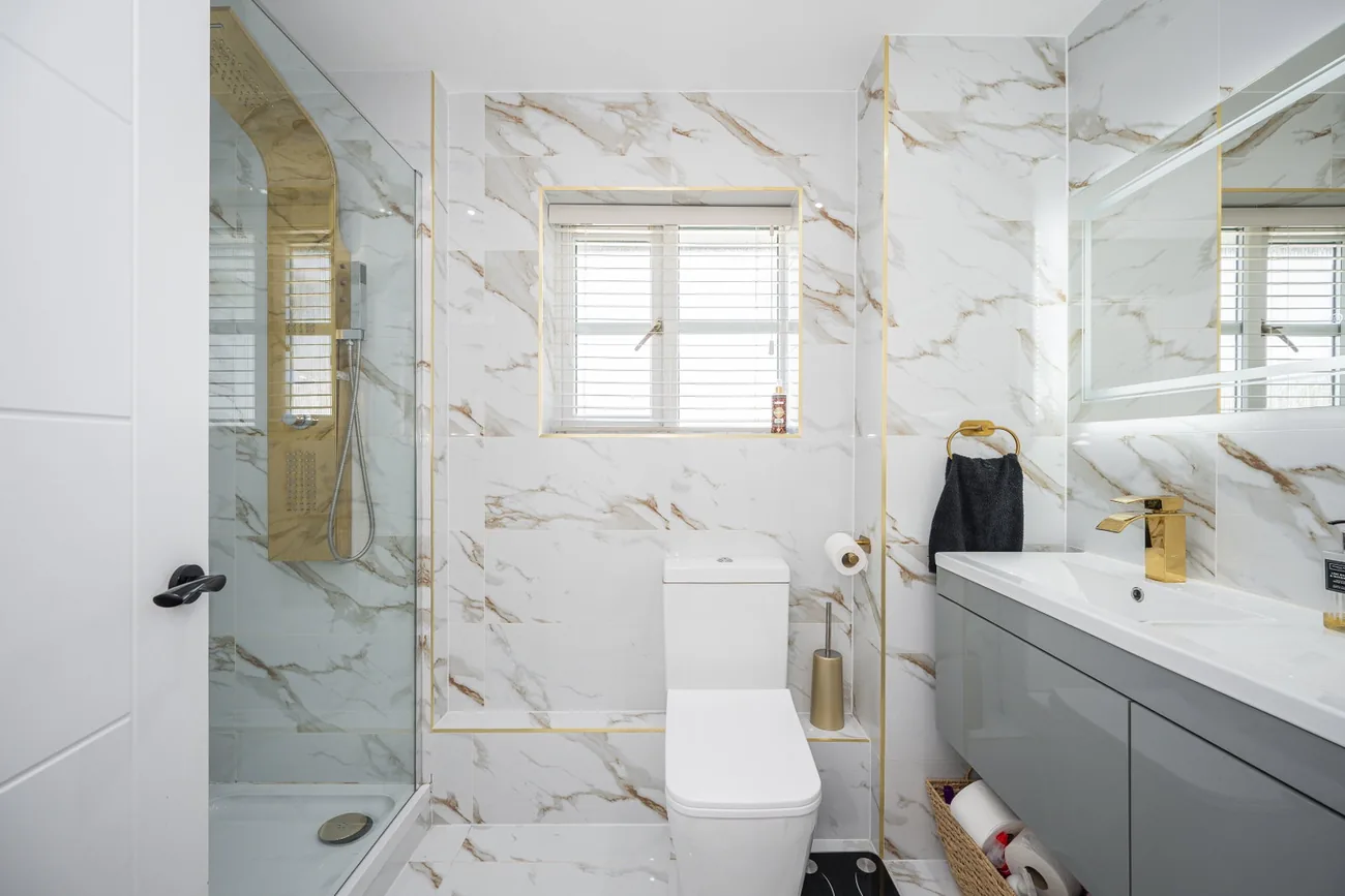En suite in marble-effect tiling with a walk-in shower and gold fittings