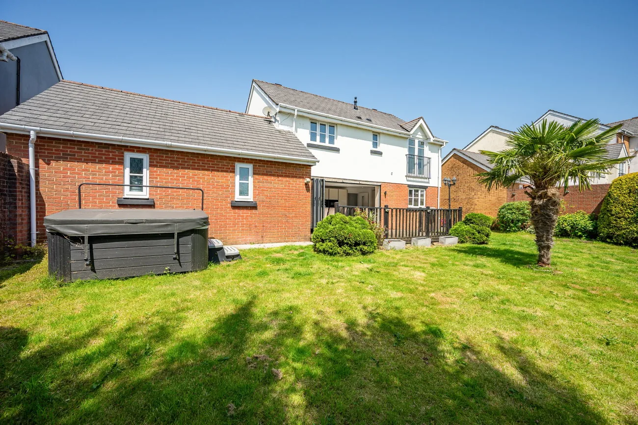Rear garden with a hot tub and lawn framed by the house