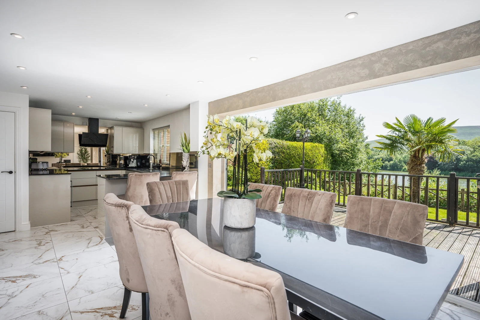 Open-plan kitchen and dining room with full-width bi-fold doors folded back onto the deck and lake view